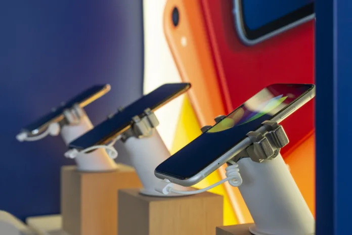 Exposição de smartphones em uma loja, fixados em suportes de segurança. Imagem ilustrativa sobre comércio de eletrônicos e fiscalização.