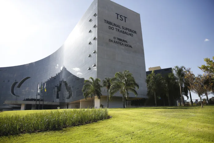 Fachada do Tribunal Superior do Trabalho (TST) em Brasília, com céu azul e área verde em primeiro plano.